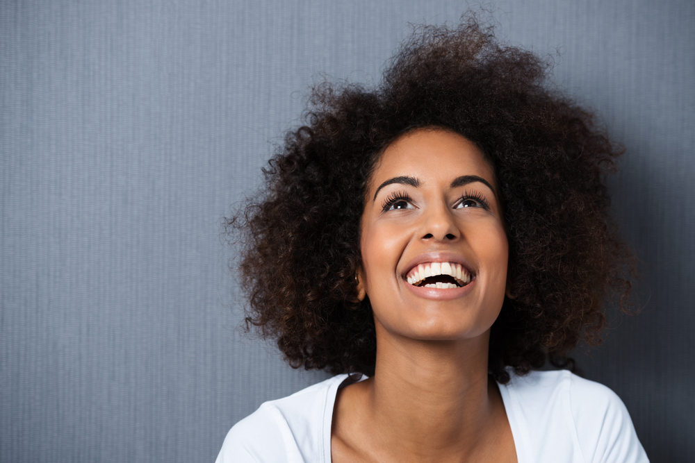 Laughing African American woman with an afro hairstyle and good sense of humor smiling as she tilts her head back to look into the air Laughing African American woman with an afro hairstyle and good sense of humor smiling as she tilts her head back to look into the air